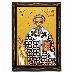 May include: An icon of Saint Clement of Rome, framed in a dark wood. The image features a man with a long white beard and a halo, wearing a patterned robe with black crosses. The text "SAINT OF" and "CLEMENT ROME" are visible.
