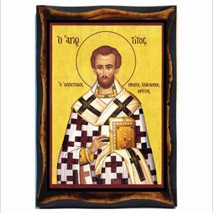 May include: A religious icon depicting Saint Titus, the first bishop of Crete. The icon is painted in a traditional Byzantine style with a gold background and features a detailed portrait of Saint Titus holding a book. The text on the icon reads "O' agios" (The Saint) and "Titus, protos episkopos Kritis" (Titus, the first bishop of Crete).