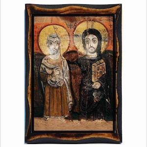 May include: An antique religious icon featuring two figures with halos, set against a faded background. The figures are depicted in traditional robes, with one holding a book. The artwork is framed in a dark, rustic wooden frame.