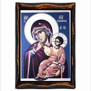 Può includere: Un'icona incorniciata che raffigura la Vergine Maria che tiene in braccio il bambino Gesù. L'icona è dipinta in uno stile tradizionale con colori vivaci, tra cui blu, rosso e oro. Il testo sull'icona recita "MP OY ПАРАМОВΙΑ IC XC".