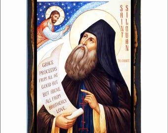 May include: A framed religious icon featuring Saint Silouan, depicted with a long beard and dark robes, looking upwards. The image includes text that reads "Grace proceeds from all at good but above all from brotherly love."