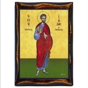 Op de afbeelding: Een religieus icoon dat de heilige Thaddeus, een christelijke apostel, afbeeldt. Het icoon is geschilderd in een traditionele Byzantijnse stijl met een gouden achtergrond en een groene basis. De heilige is afgebeeld in een rode mantel met een blauwe onderkleed, een rol in zijn linkerhand houdend en een zegengebaar met zijn rechterhand makend. Het icoon is ingelijst in een donkerhouten lijst.
