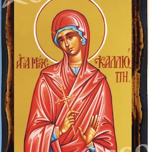 Puede incluir: Un icono religioso que representa a una mujer con una túnica roja sosteniendo una cruz. El fondo es dorado y el texto dice "Santa Kalliope".