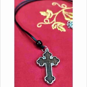 Può includere: Un ciondolo a forma di croce in argento e legno su una collana con cordoncino nero. La croce ha un design dettagliato ed è un simbolo religioso.
