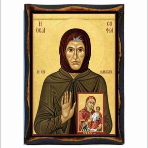 Può includere: Icona religiosa raffigurante una donna con un velo e una veste marrone, con un'aureola. Tiene in mano una piccola icona raffigurante una donna e un bambino. L'opera è incorniciata in una cornice di legno scuro.