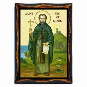 May include: A framed religious icon depicting Saint Erc of Slane. The image shows a man in green robes holding a cross and scroll, with a halo. The background features a church on a hill, the sea, and three fish.