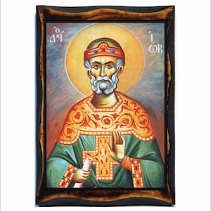 May include: A hand-painted icon of a bearded man wearing a crown and green and gold robes. He is holding a scroll in his left hand and his right hand is raised in blessing. The icon is set against a yellow halo and a blue and gray background. The text "Ο Άγιος" and "Ιωάννης" is visible in the top corners of the icon.