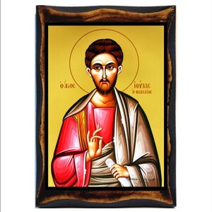 Op de afbeelding: Een religieus icoon van Johannes de Doper, geschilderd in traditionele Byzantijnse stijl. Het icoon heeft een gouden achtergrond met een halo rond het hoofd van de heilige. Hij wordt afgebeeld met een lange baard en draagt een rode en witte robe. Het icoon is ingelijst in een donkerhouten lijst.