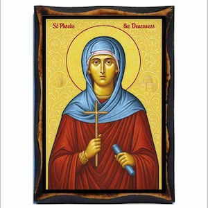 May include: An icon of St. Phoebe the Deaconess, featuring a woman in a blue head covering and red robes, holding a cross and a scroll. The image has a gold halo and is set in a dark wooden frame.