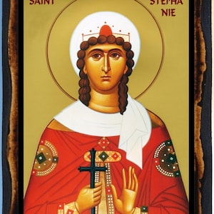 May include: A religious icon depicting Saint Stephania, a woman with a crown and a cross, against a gold background. The icon is framed in a dark wood frame.