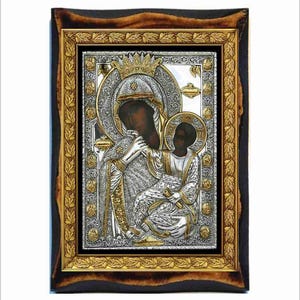 Può includere: Un'icona incorniciata in argento e oro che rappresenta la Vergine Maria e il bambino Gesù. L'icona è su sfondo nero e presenta dettagli intricati.