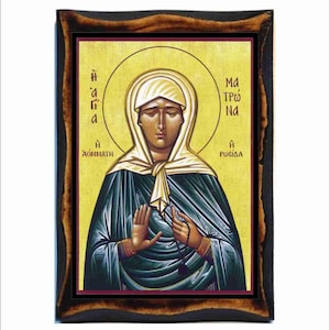 May include: A religious icon of a woman with a halo, wearing a blue robe and white head covering. The icon is framed in a dark wood frame. The text on the icon reads "Η Ἁγία" and "Η Ροσίδα".
