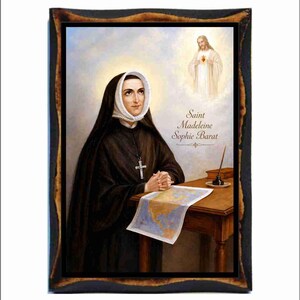 Könnte beinhalten: Gerahmtes Porträt von Saint Madeleine Sophie Barat, dargestellt in einem schwarzen Habit und weißer Kopfbedeckung, mit einer Kreuzkette. Der Text "Saint Madeleine Sophie Barat" ist enthalten. Eine Karte und ein Tintenfass befinden sich auf dem Holztisch.
