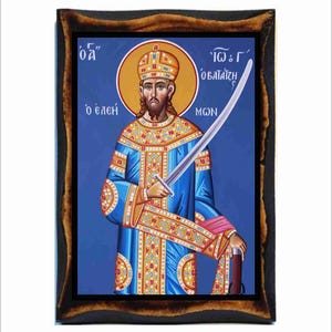 Op de afbeelding: Een religieus icoon dat een man in een blauwe robe en een gouden kroon afbeeldt, die een zwaard vasthoudt. Het icoon heeft een blauwe achtergrond en een houten frame. De tekst op het icoon luidt "'Iω's' 'oβασιλiζη' 'MωN'" en "'oδ' 'o ελεη'"