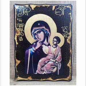 Può includere: Un'icona religiosa che raffigura la Vergine Maria che tiene in braccio il bambino Gesù. L'icona è dipinta su un pannello di legno con una finitura in vernice nera invecchiata e screpolata. La Vergine Maria indossa una veste blu e viola, e il bambino Gesù indossa una veste rosa. L'icona è incorniciata in una cornice dorata.