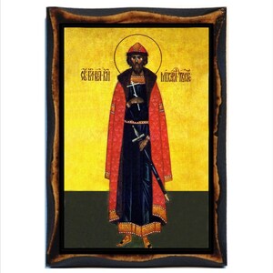 May include: A religious icon depicting Saint Michael, a warrior saint, in a red robe and black tunic, holding a sword. The icon has a gold background and a wooden frame.