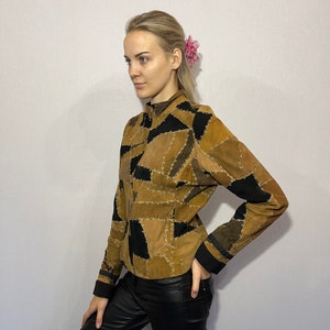 Op de afbeelding: Een bruin en zwart patchwork suède jack met lange mouwen en een opstaande kraag.