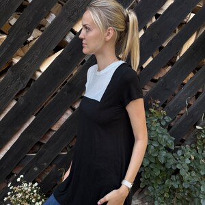 May include: A woman wearing a black and white tunic top with short sleeves. The top has a white panel across the chest and a black panel below. She is wearing blue jeans and a silver watch.