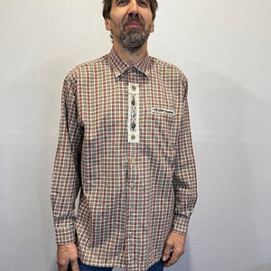 May include: A long-sleeved plaid shirt in beige, red, and green. The shirt features decorative embroidery and buttons down the front. The shirt is paired with blue jeans.