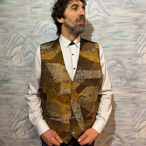 Può includere: Un gilet in pelle scamosciata marrone con un design a patchwork che presenta una stampa vintage di una mappa del mondo. Il gilet ha una chiusura con bottoni e due tasche.