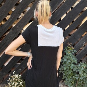 May include: A black and white t-shirt with a white panel on the back. The shirt has short sleeves and a relaxed fit.