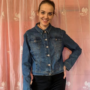 Könnte beinhalten: Eine blaue Jeansjacke mit Knopfleiste und zwei Taschen auf der Vorderseite.