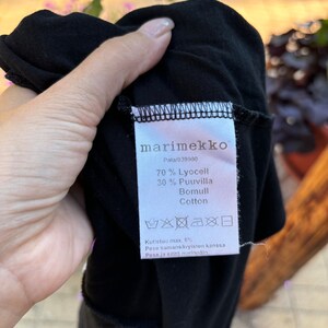May include: Black marimekko clothing label with white text. The label says "70% Lyocell 30% Puuvilla Bomull Cotton" and "Kutistuu max. 6% Pese samans&auml;vyisten kanssa Pese ja silită nurino&scaron;in".