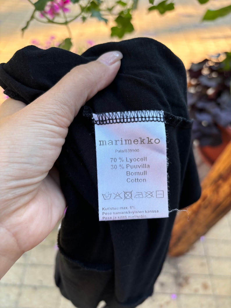 May include: Black marimekko clothing label with white text. The label says "70% Lyocell 30% Puuvilla Bomull Cotton" and "Kutistuu max. 6% Pese samans&auml;vyisten kanssa Pese ja silită nurino&scaron;in".