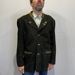 May include: Dark green suede jacket with a notched collar and decorative buttons. The jacket has two front pockets with brown trim and a brown collar. The jacket is worn over a light blue shirt with a floral design. The person is wearing blue jeans.