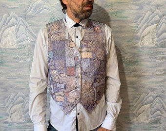 May include: A patterned vest with a floral design in shades of purple, tan, and white. The vest has a button-up front and is worn over a white collared shirt and blue jeans. The vest appears to be made of a lightweight fabric.