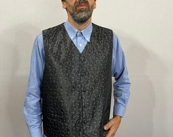 May include: A black vest with a subtle floral pattern, worn over a light blue button-down shirt and blue jeans. The vest has a five-button closure and a textured appearance, creating a classic and stylish look.