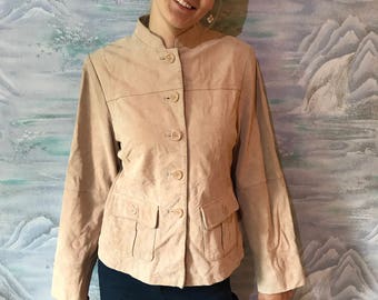 Könnte beinhalten: Eine hellbraune Wildlederjacke mit einem Stehkragen und mehreren Knöpfen auf der Vorderseite. Die Jacke hat zwei Pattentaschen auf der Vorderseite und lange Ärmel.