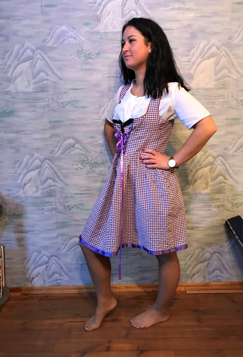 May include: A purple and white checkered dress with a white blouse underneath. The dress has purple ribbon accents and trim. The person is wearing a watch.