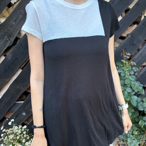 May include: A black and white t-shirt with a contrasting color block design. The top half of the shirt is white, and the bottom half is black.