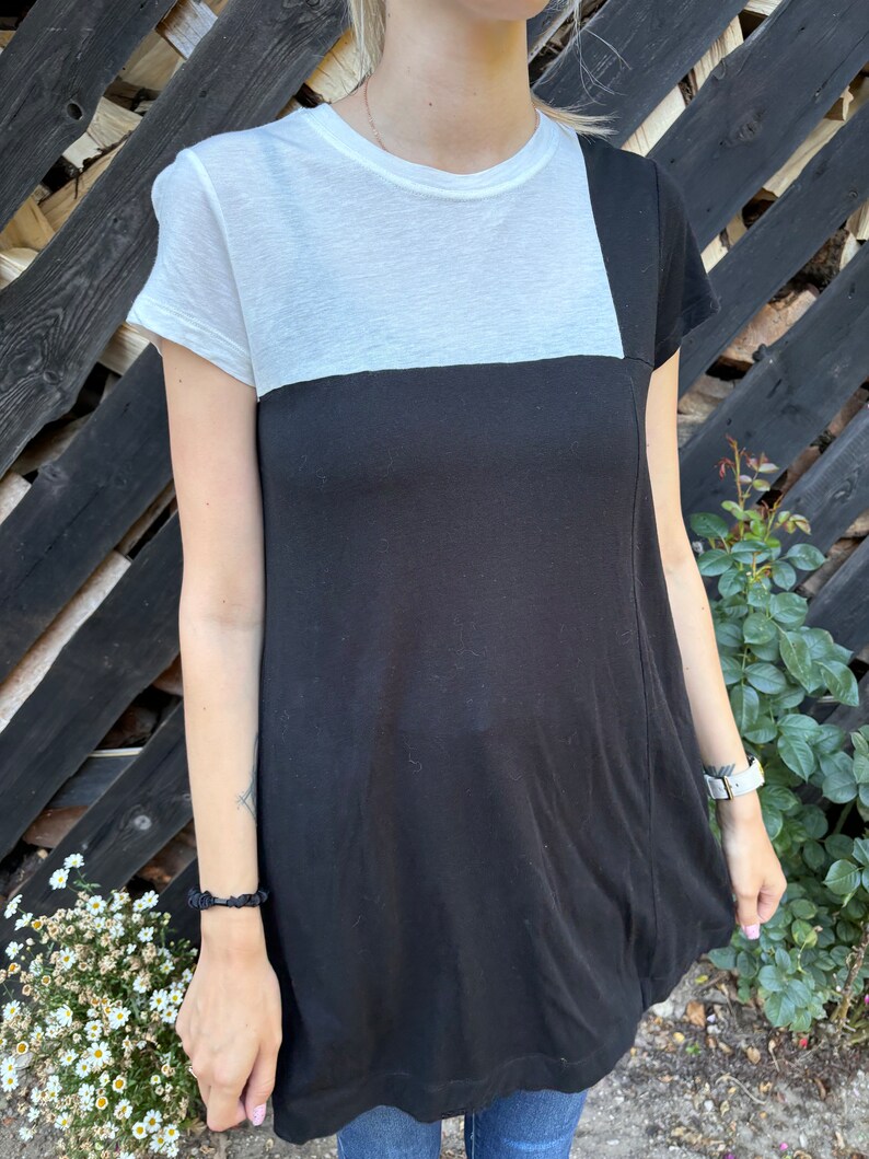 May include: A black and white t-shirt with a contrasting color block design. The top half of the shirt is white, and the bottom half is black.