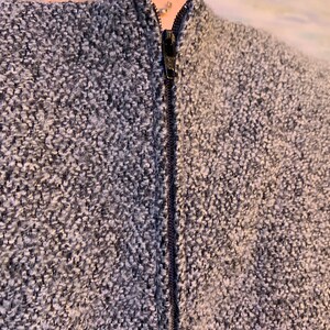 May include: Close-up of a textured grey and white fabric with a black zip down the centre. The fabric appears to be a woven material, possibly part of a jacket or coat.