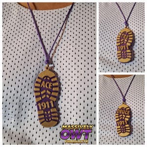 May include: A purple and gold pendant necklace with a shoe print design. The pendant has the word "ACE" and the number "1911" on it. The necklace is on a purple cord.