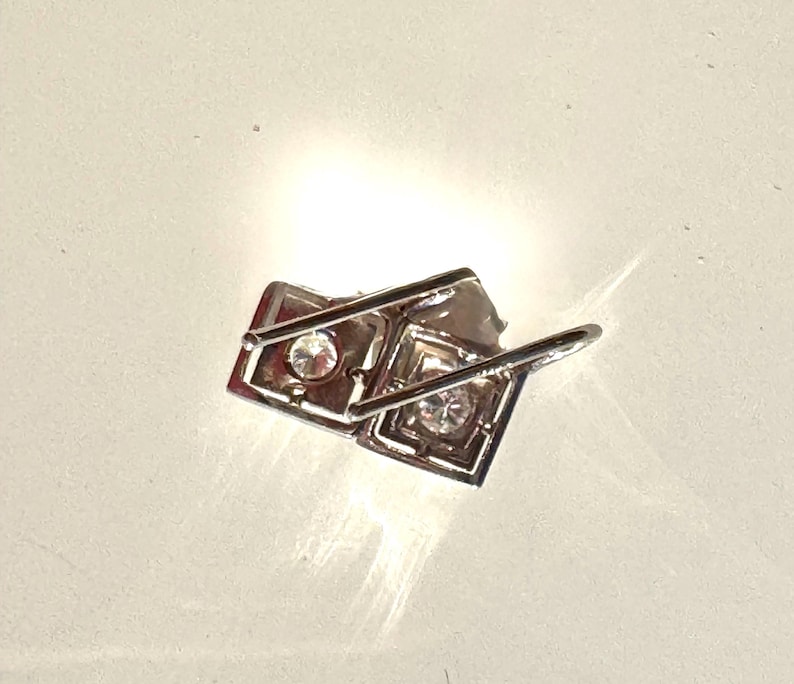 May include: Silver earrings with two square-shaped settings, each with a clear rhinestone in the center.