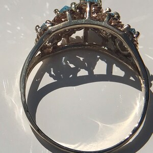 May include: A silver ring with a delicate design featuring multiple blue gemstones. The ring is set with a row of stones in the center and smaller stones on either side.