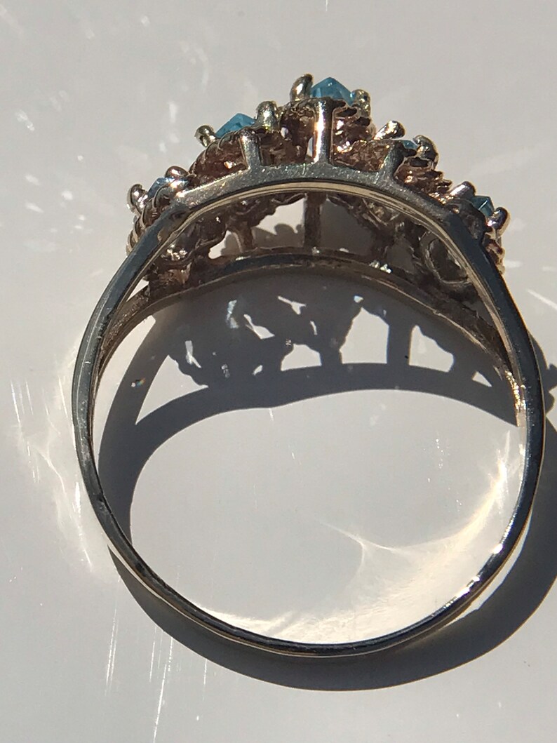 May include: A silver ring with a delicate design featuring multiple blue gemstones. The ring is set with a row of stones in the center and smaller stones on either side.