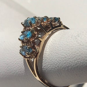 May include: A gold ring with a cluster of blue topaz gemstones set in a delicate, intricate design.