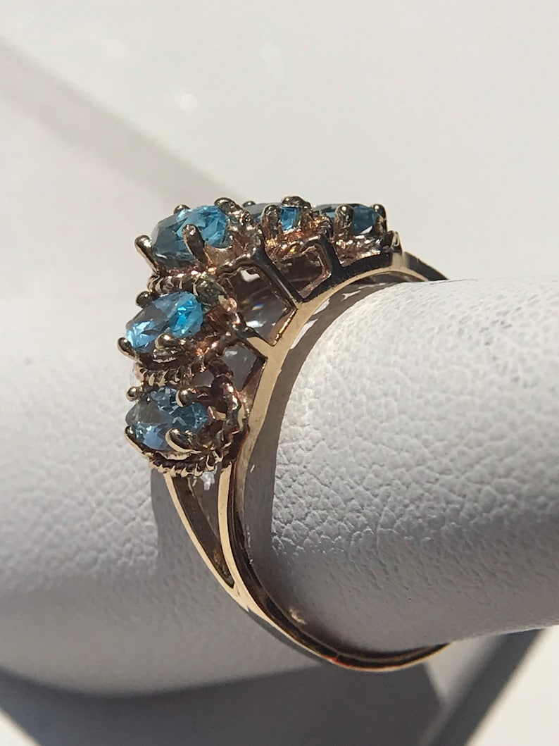 May include: A gold ring with a cluster of blue topaz gemstones set in a delicate, intricate design.