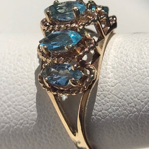 May include: A gold ring with three marquise-shaped blue topaz gemstones set in a rope-like design.