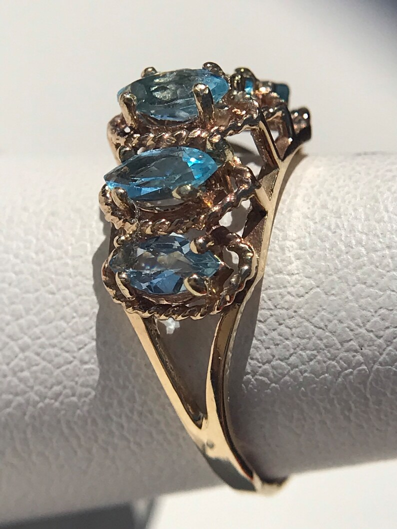 May include: A gold ring with three marquise-shaped blue topaz gemstones set in a rope-like design.