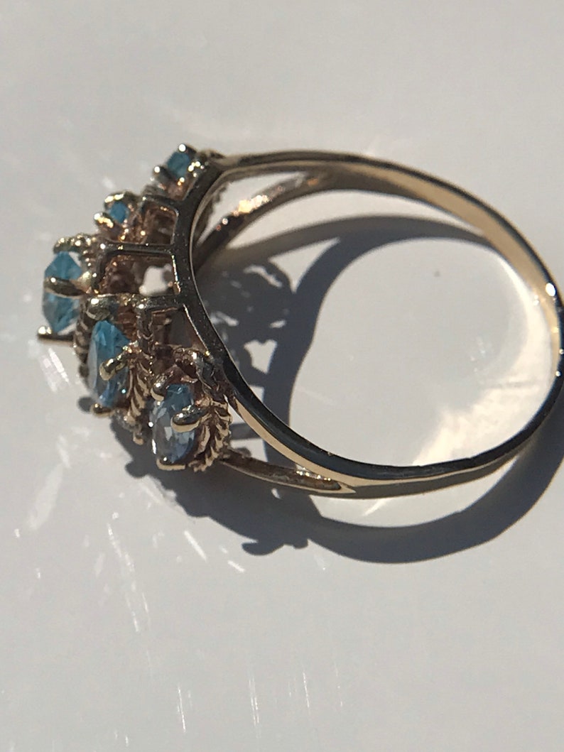 May include: A gold ring with a row of blue gemstones set in a delicate, intricate design.