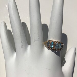May include: A gold ring with a row of oval-shaped blue gemstones set in a delicate, twisted band.