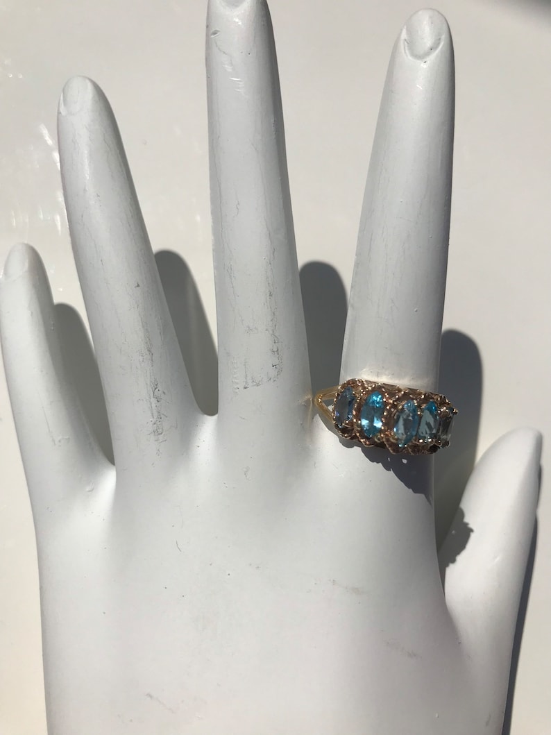 May include: A gold ring with a row of oval-shaped blue gemstones set in a delicate, twisted band.