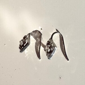 May include: A pair of silver dangle earrings with a clear crystal stone in the center of each earring.