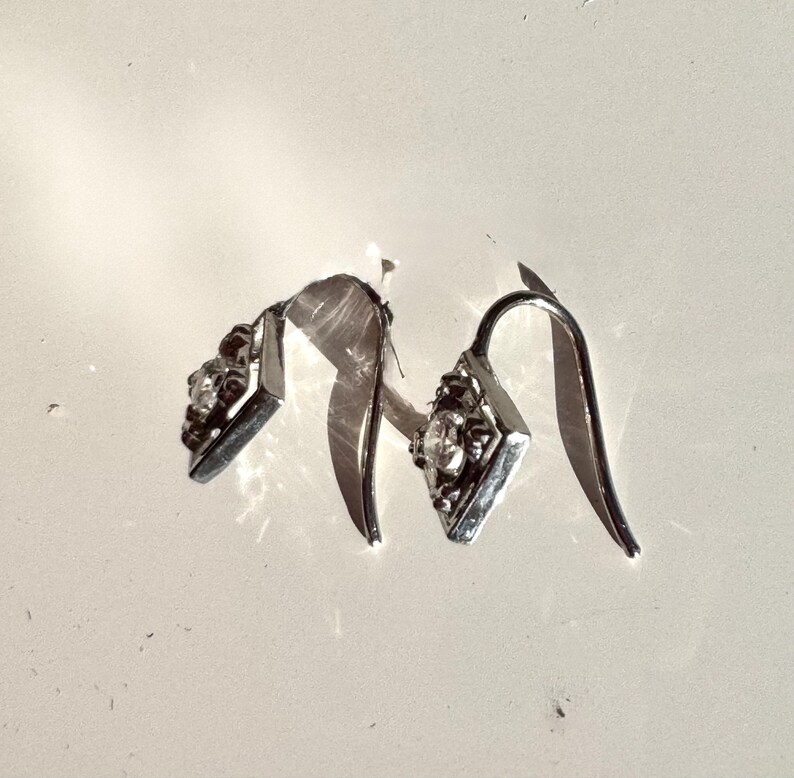 May include: A pair of silver dangle earrings with a clear crystal stone in the center of each earring.