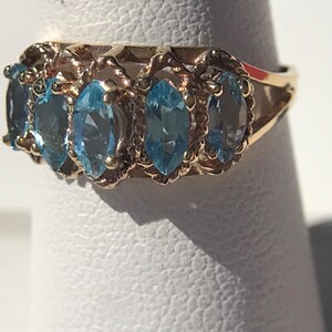 May include: A gold ring with five blue topaz stones set in a delicate, twisted band.
